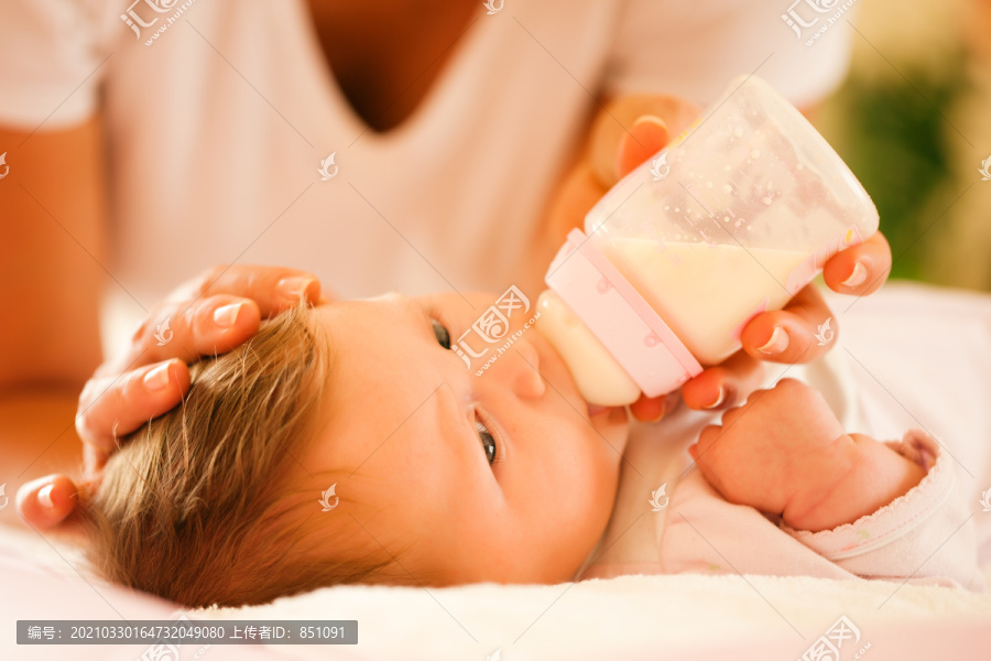母亲-只有手和躯干可以看到-正在用奶瓶喂养她的婴儿