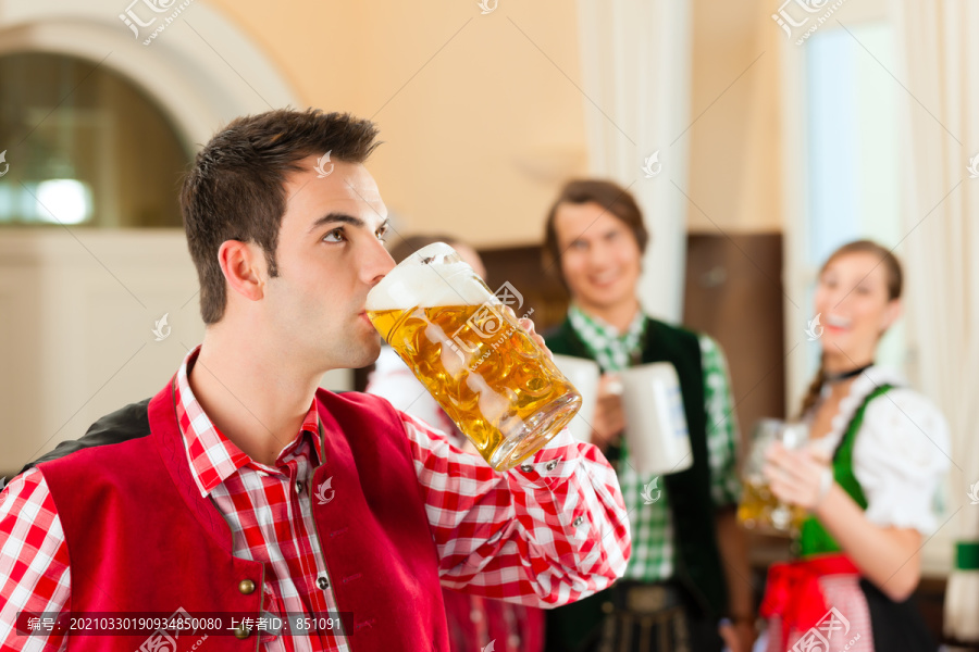 年轻人在传统的巴伐利亚州餐馆或酒吧里，一名男子正站在与啤酒史坦在前面，该集团的背景