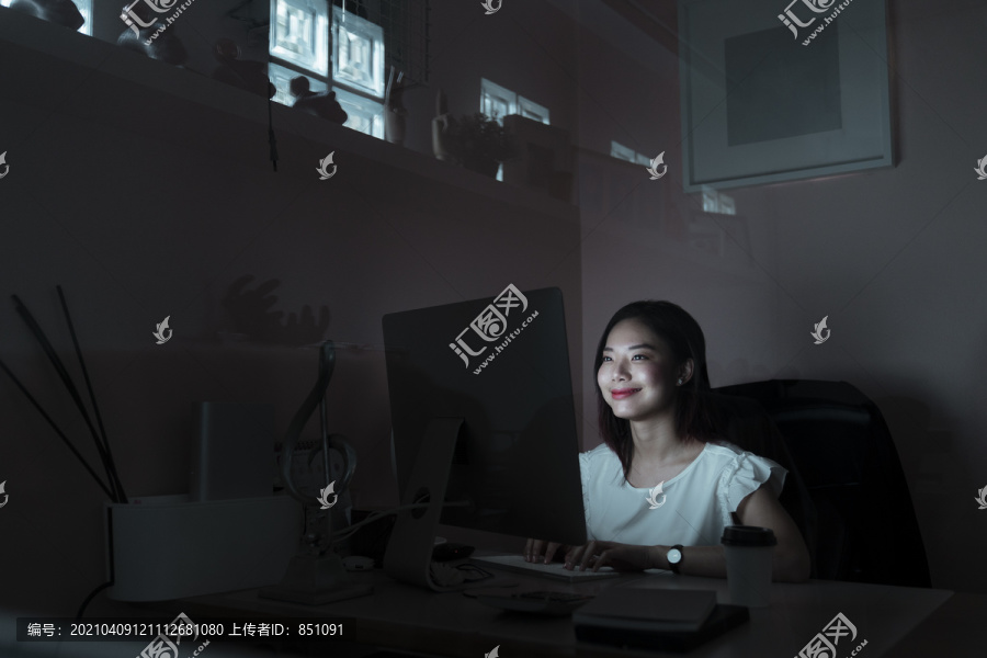 微笑年轻的亚洲女人对自己的工作结果感到满意，工作到午夜——加班。