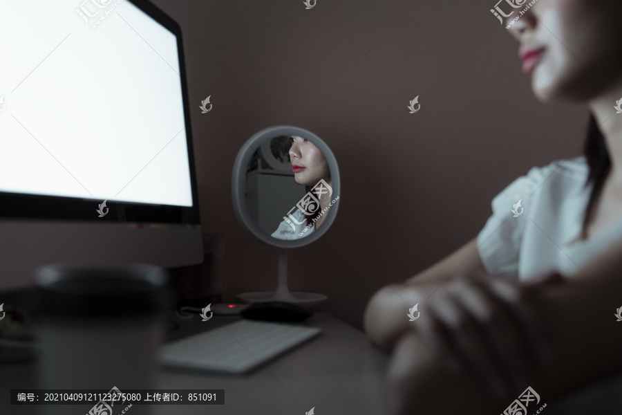 晚上加班的女人对着电脑微笑。镜子反映出她的表情。情感和表达。