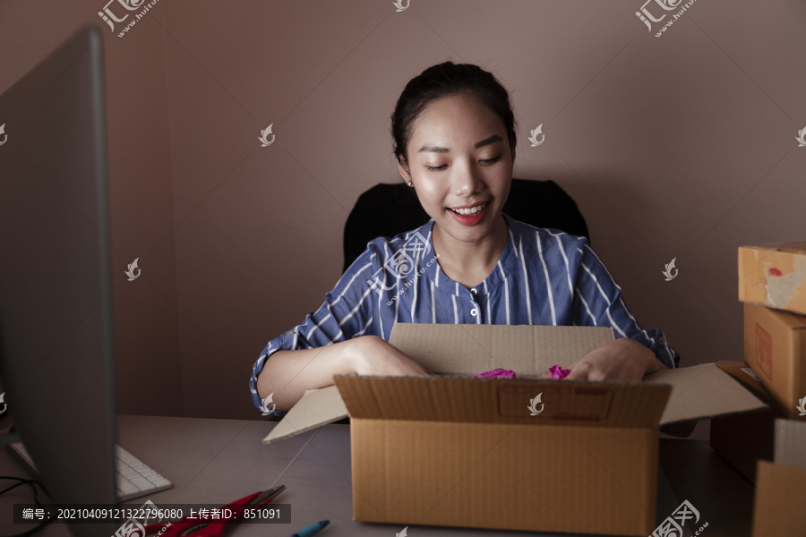 快乐的亚泰妇女在电脑前打开装运箱。