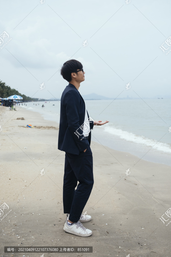 黑发黑衣人站在沙滩上伸手看海。