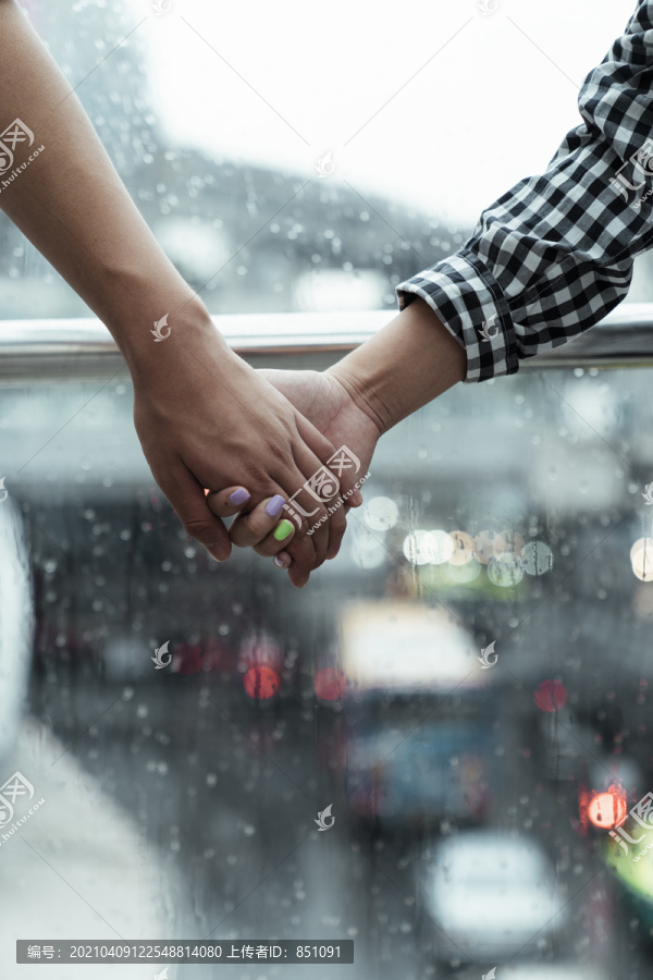 一对夫妇的手紧紧握在玻璃上的雨水作为背景的特写镜头。