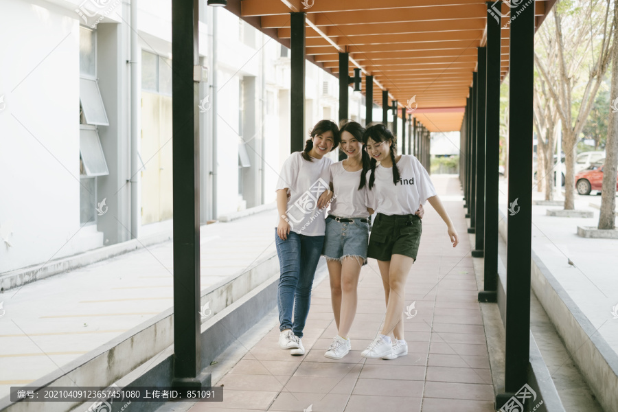 三个穿着白色休闲衬衫的泰国亚裔学生在学校散步，互相拥抱。