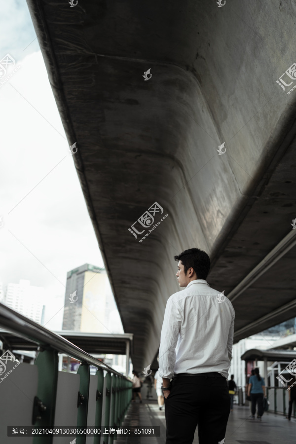 一位穿着白色正式衬衫的成熟亚洲商人走在人行道上，沿路眺望。
