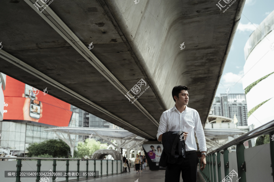 一位穿着白色正式衬衫的成熟亚洲商人下班后走在天桥上。