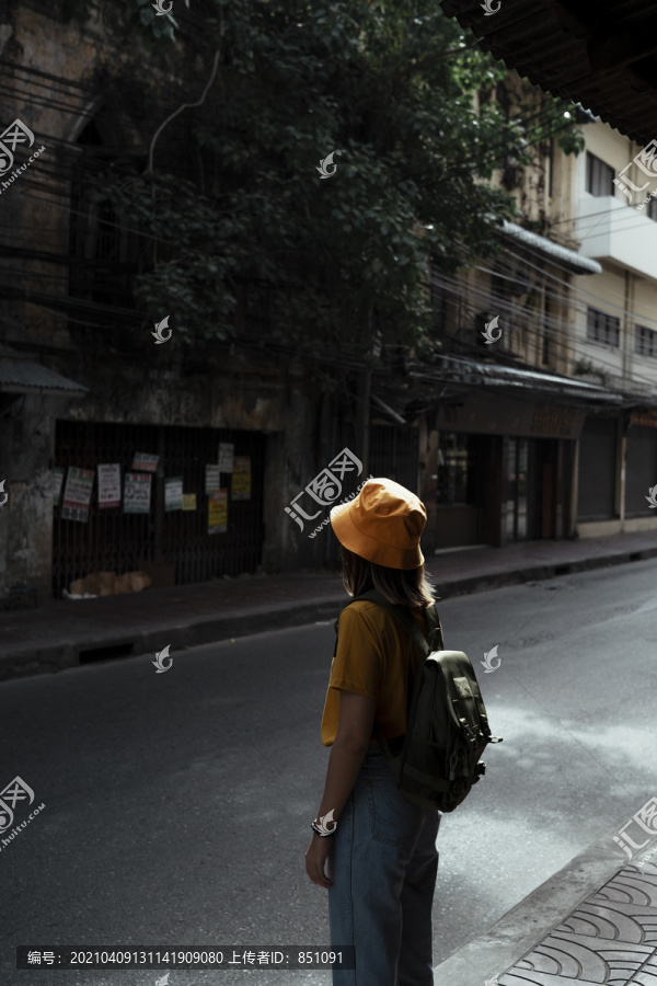 黄色的背包女，背着绿色的背包，站在古色古香的老城路边。