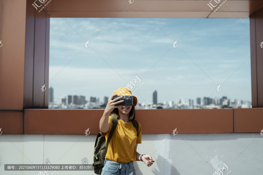 带着绿色背包的黄色背包客用智能手机与城市景观自拍。