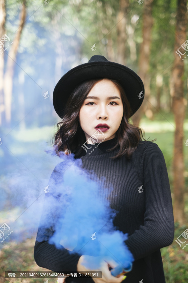 一个穿着黑色衣服的女巫在森林里玩蓝色的烟火。