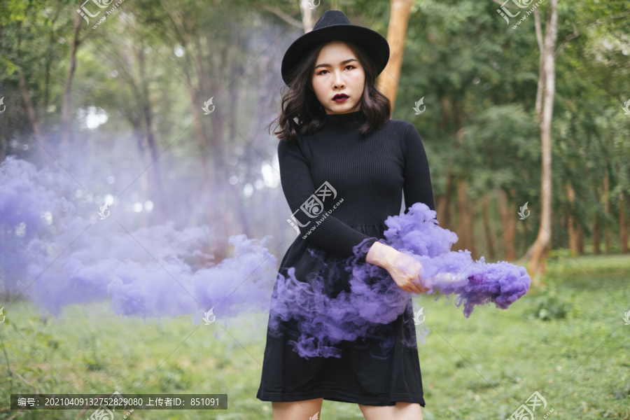 一个穿着黑色衣服的女孩直视镜头，目光敏锐，手里拿着紫色的烟火。