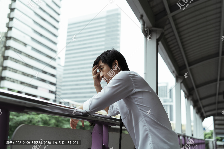 悲伤的泰国年轻商人站在天桥上，双手靠在扶手上望着外面的路。辞职后的泰国年轻人生意压力很大。