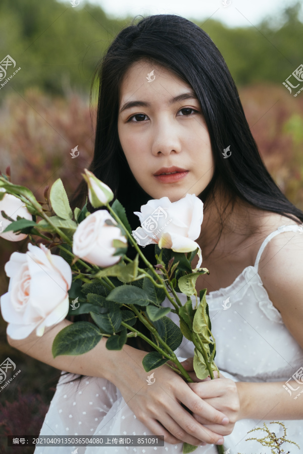 特寫-年輕的亞洲長黑發(fā)女子新娘手持白玫瑰花坐在田野里的肖像。復(fù)古的。