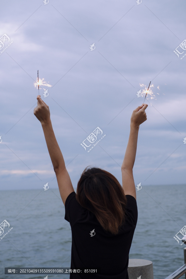 背景图：年轻的泰国亚裔女子短发举手举着两个火花头在海滩上在杜什时间。