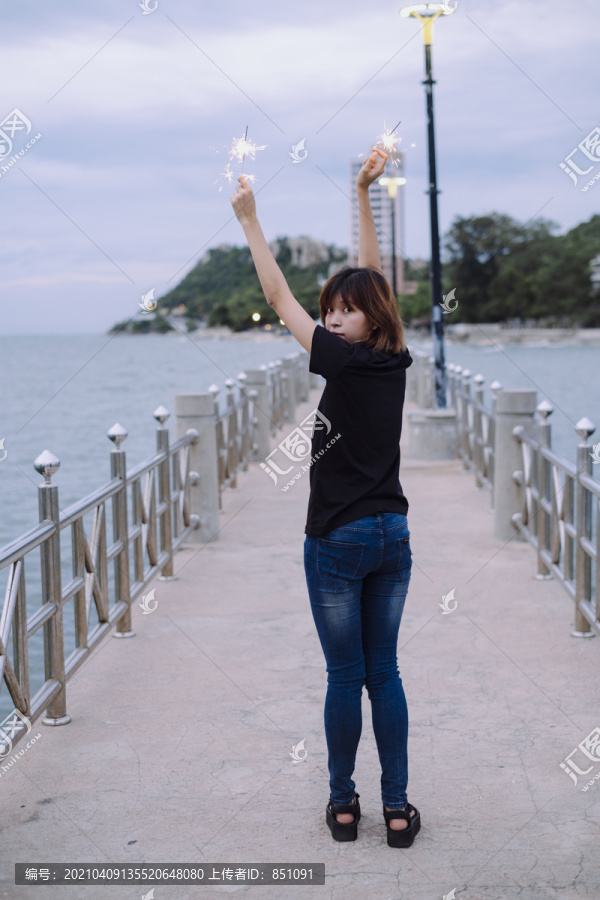苗条的女孩。杜什时间，一位年轻的泰国亚裔女子双手捧着两个火花在海边散步。