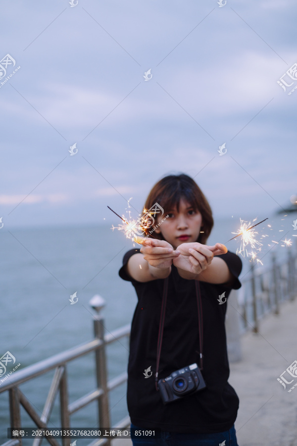 年轻的亚洲短发女子拿着两个火花在沙滩上玩耍的肖像。