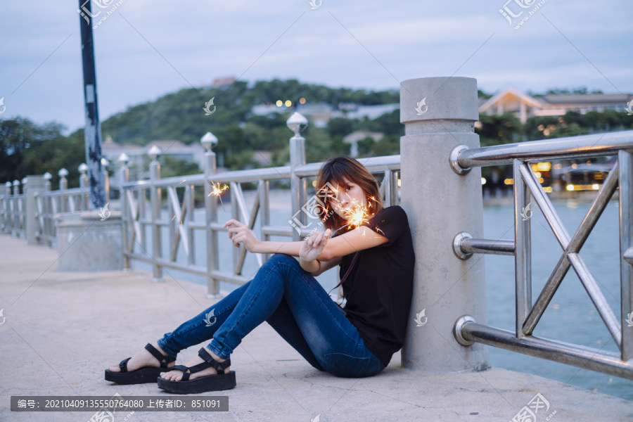 年轻的泰国亚裔女子短发坐在海桥上玩火花在黄昏时间。