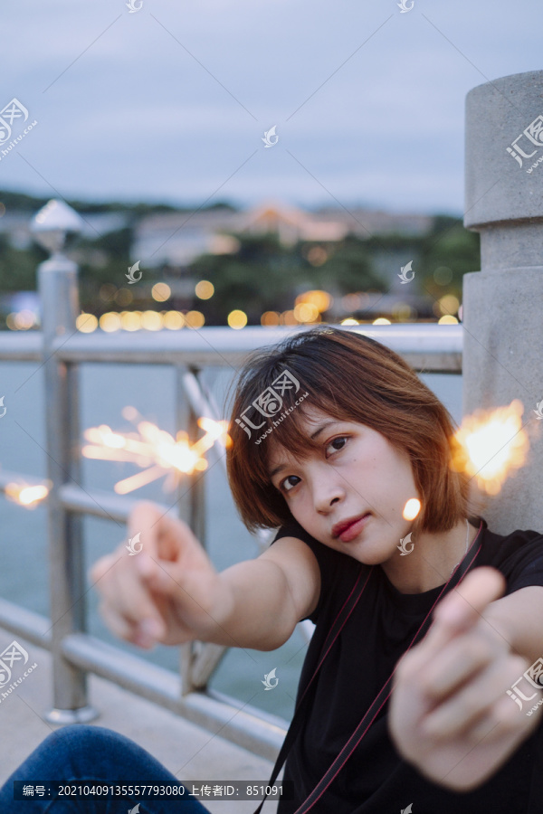 年轻的泰国亚裔女子短发坐在海桥上玩火花在黄昏时间。