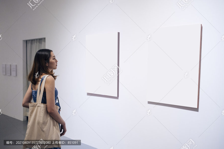 美丽的亚洲年轻女子在美术馆里看着空白的纸画布。