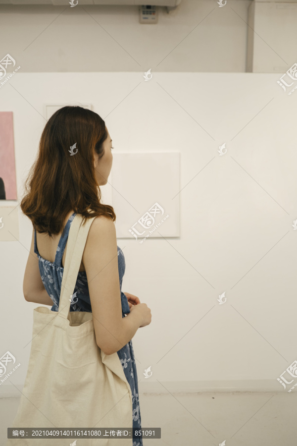 后视图中的妇女在蓝色的衣服看美术架在画廊。