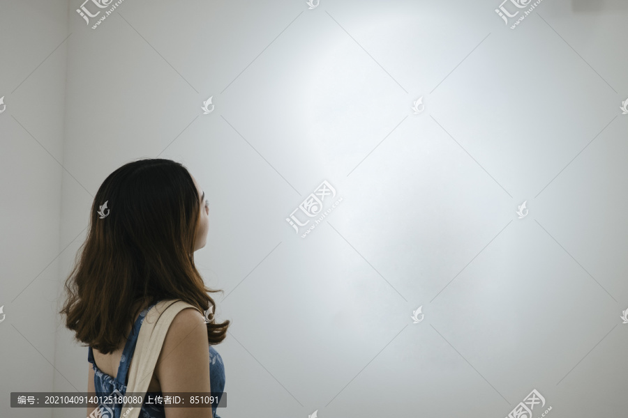 一个女人在美术馆里看着白色的空镜框。