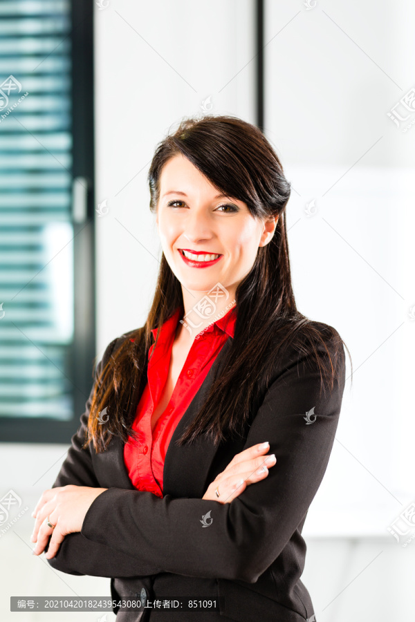 一个穿着商务服的女商人在办公室的肖像，她对着镜头微笑