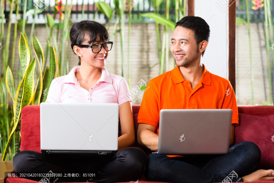 印尼的一对年轻夫妇坐在沙发上，手里拿着笔记本电脑，也许他们有什么想法或灵感