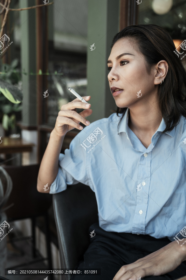 特写一位身着蓝色连衣裙的亚泰妇女坐在椅子上抽烟，看上去很酷。