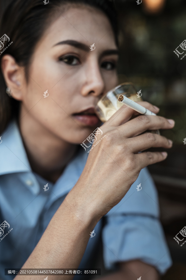 特写身着蓝色连衣裙的亚泰妇女抽烟喝咖啡。