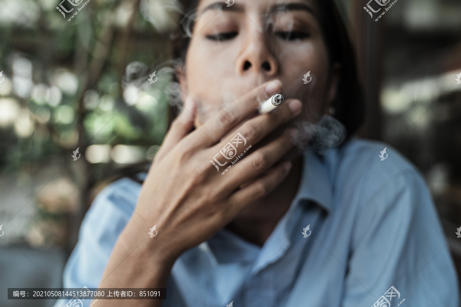 特写身着蓝色连衣裙在户外吸烟的亚泰妇女的脸。