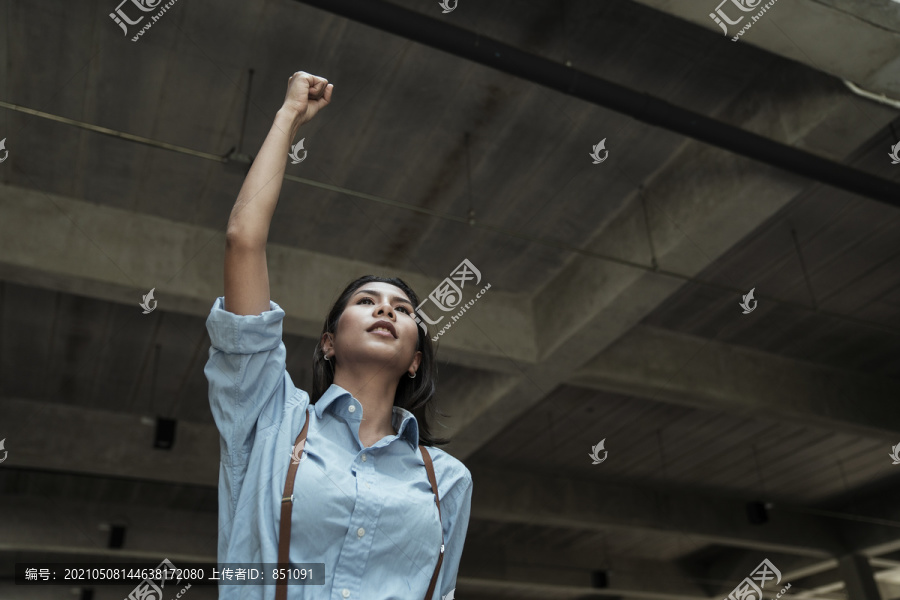 身着蓝色连衣裙的泰国亚裔女子举起手臂。胜利与成功。