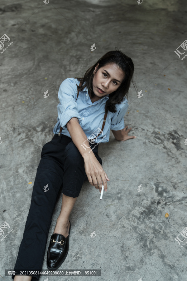 穿着蓝色衬衫的泰国亚裔女子躺在地上抽烟。