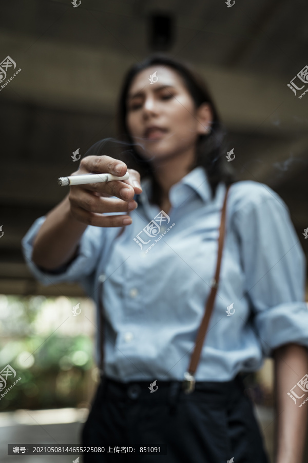 穿着蓝色衬衫、满脸愁容的亚洲女人拿着香烟指着镜头。