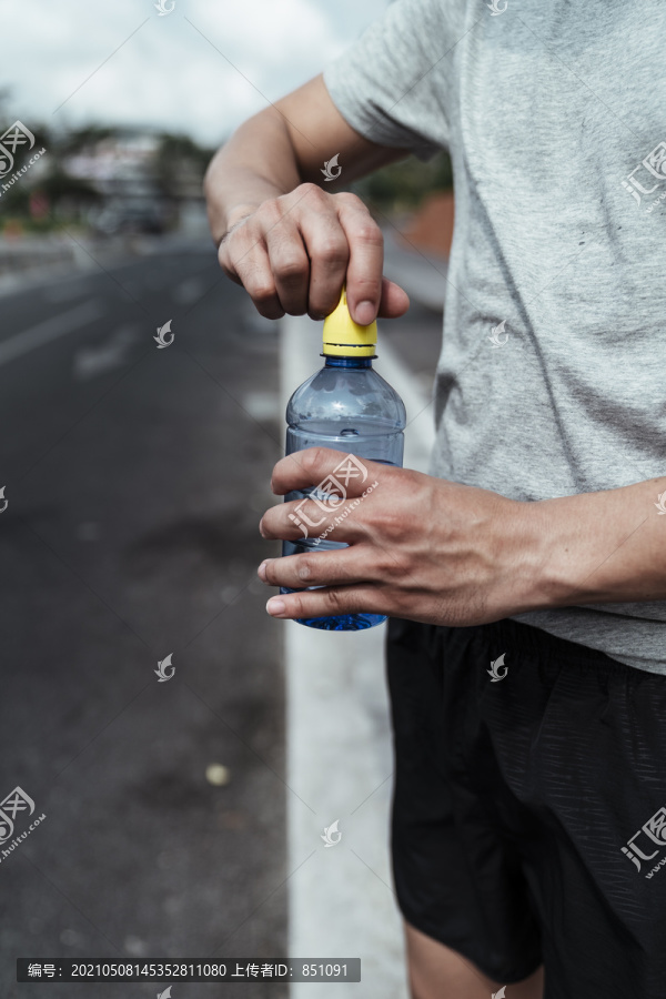 运动员年轻人跑累后打开一瓶水。