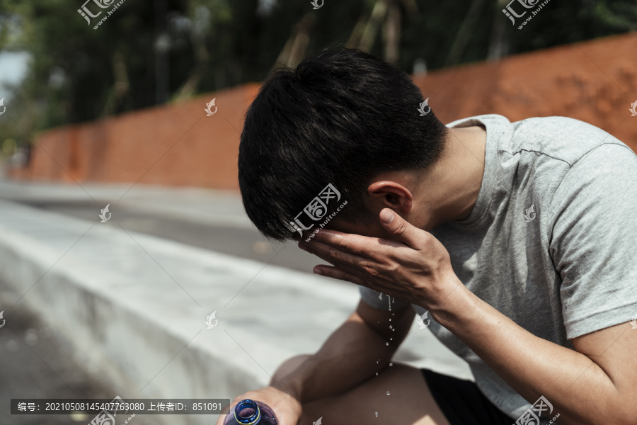 运动男用瓶子里的水洗脸。亚洲年轻人用瓶子里的水洗脸。