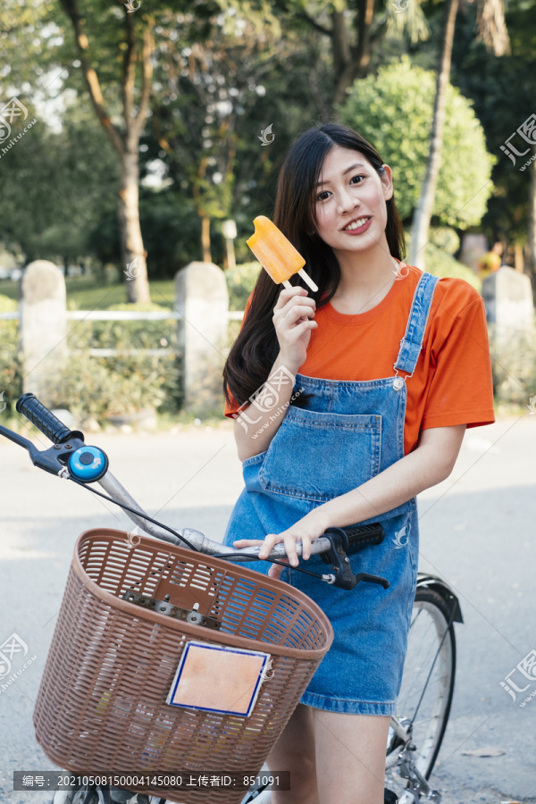 身着橙色t恤和牛仔裤套头衫的长发女孩展示自行车上的橙色冰淇淋。