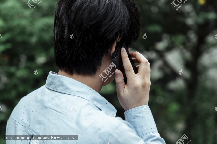 一个穿着蓝衬衫的黑发男人站在花园里给女朋友打电话。