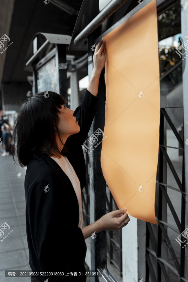 年轻的泰国亚裔女子深色短发站在街上橙色的空白纸上。