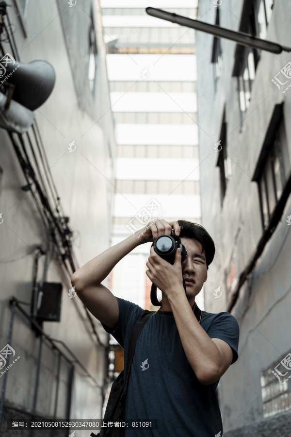 年轻英俊的亚洲摄影师男子手持相机在城市街道小巷拍照。