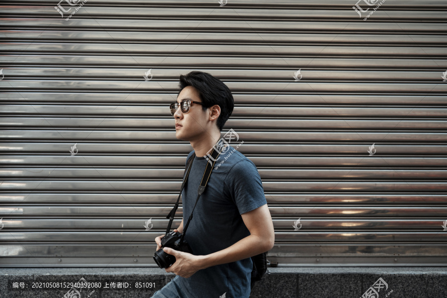 年轻英俊的亚洲摄影师戴着墨镜走在街上。拿着相机的男人。