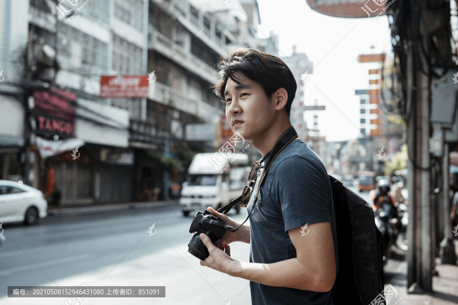 年轻英俊的亚洲摄影师走在街上用相机拍照。街头摄影。