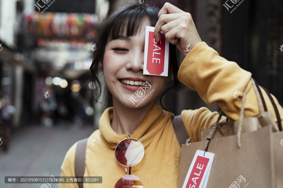 美丽的亚洲女人穿着黄色毛衣，背着许多贴着价签的购物袋，走在街上。