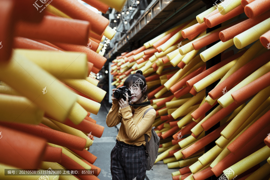 一位身穿黄色毛衣的亚洲年轻女子手持相机在街巷的嘉年华活动中拍照。