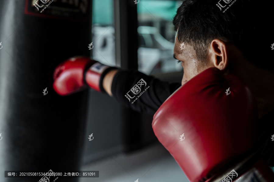 亚泰体育男子戴红手套打孔沙袋。在体育馆练习泰拳。