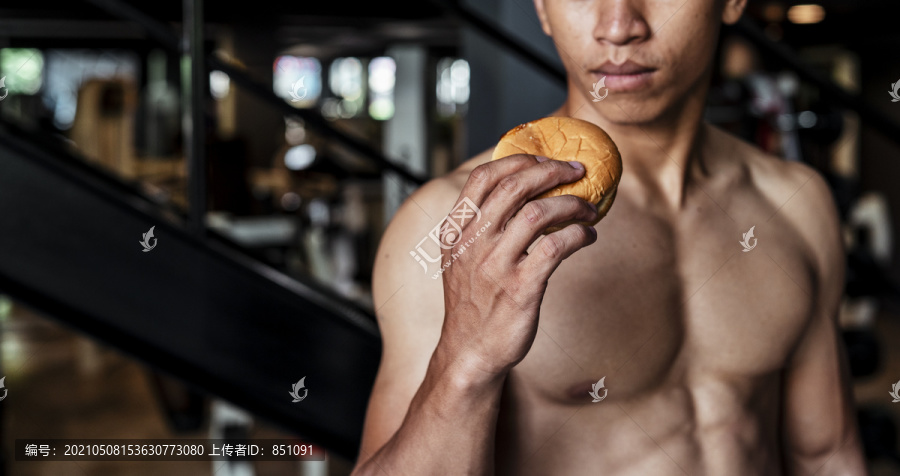 运动员亚泰体育男子拿着奶酪汉堡包决定吃还是不吃。健身房背景。
