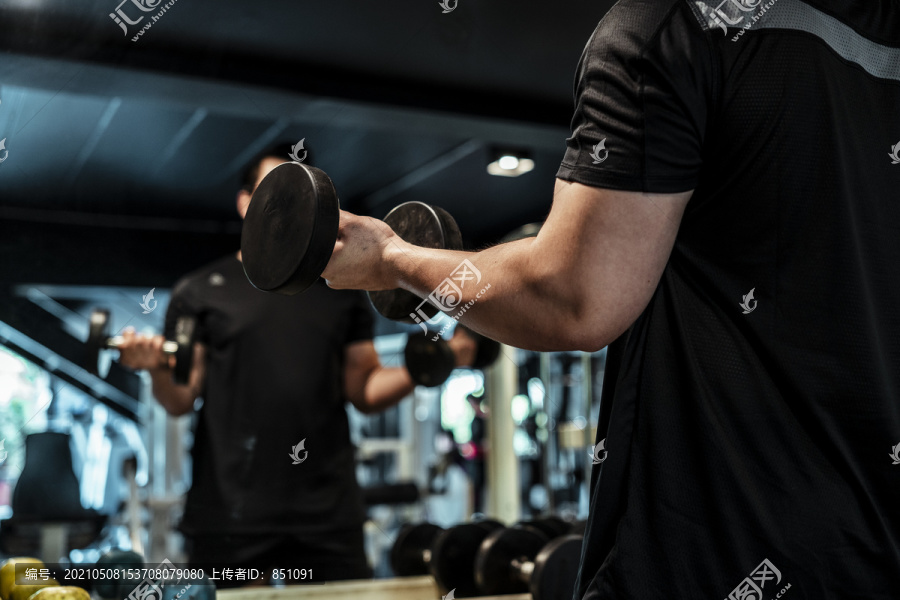 运动员亚泰运动员在健身房对着镜子练习哑铃。
