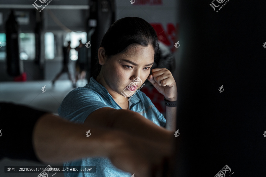 穿着蓝色运动服的亚洲胖女人在健身房练习带沙袋的泰拳。