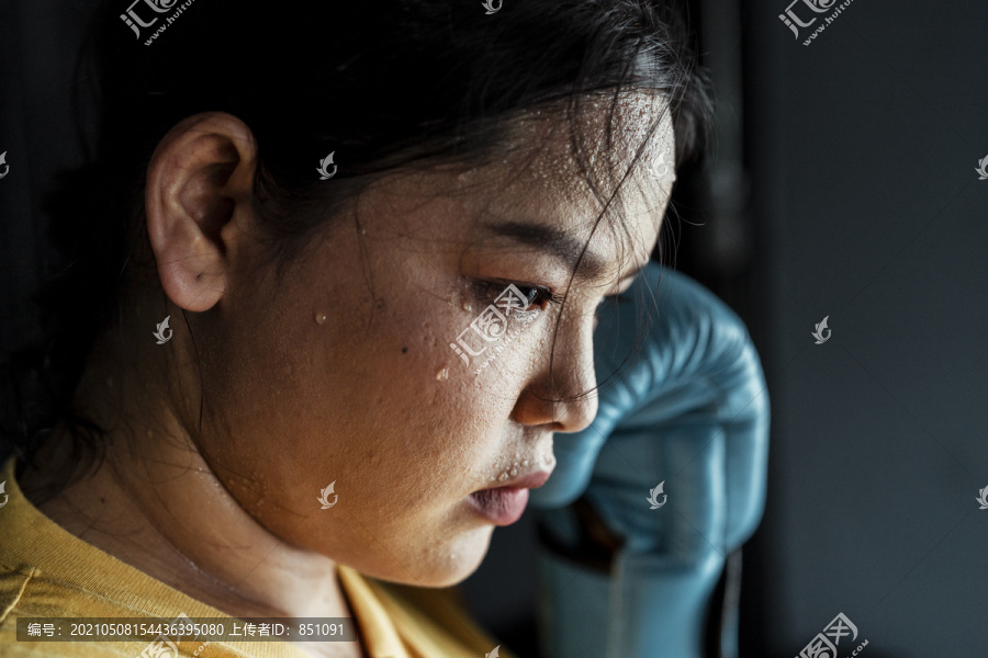 特写胖乎乎的运动型亚洲女人穿着黄色运动服和蓝色拳击手套在健身房锻炼。