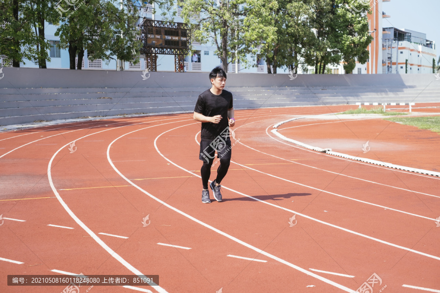 运动亚泰男子身穿黑色运动服慢跑或在体育场内跑道上跑步。
