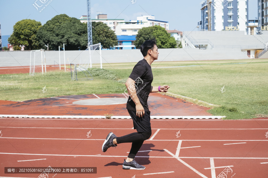 运动亚泰男子身穿黑色运动服慢跑或在体育场内跑道上跑步。