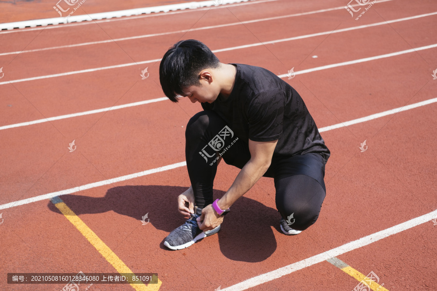 一名身穿黑色运动服的亚泰男子在跑道上跑步后系鞋带。